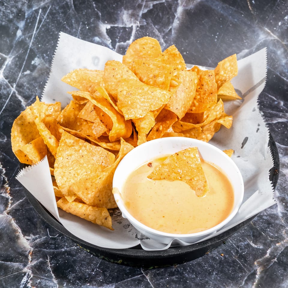 Basket of seasoned tortilla chips with creamy dipping sauce on a black marble tabletop.