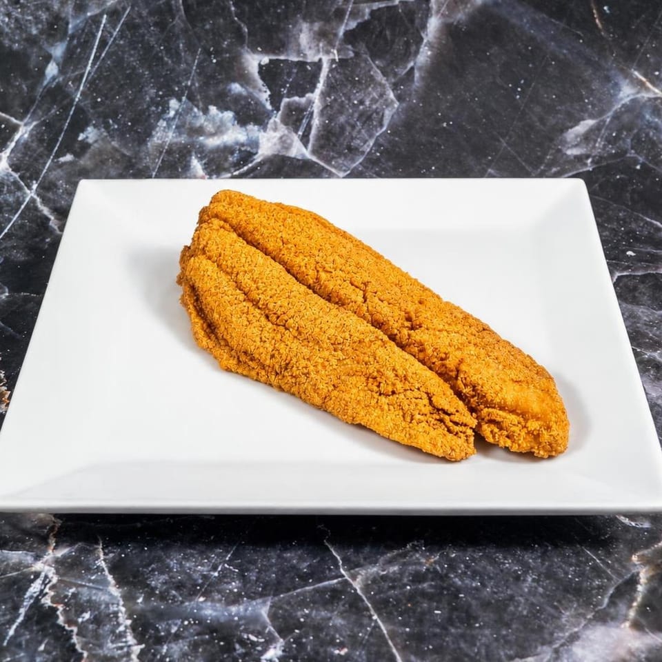 Three golden, crispy fried fillets arranged on a white rectangular plate over a black marble countertop.